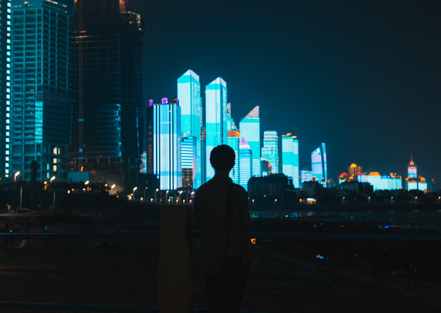 silhouette of man admiring bright lights of skyscrapers